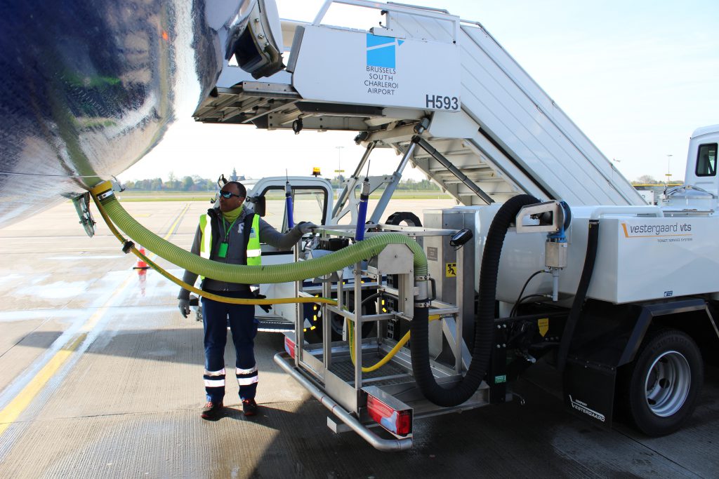 Fueling truck connected to an aircraft, with a worker in safety gear operating the equipment on an airport tarmac.