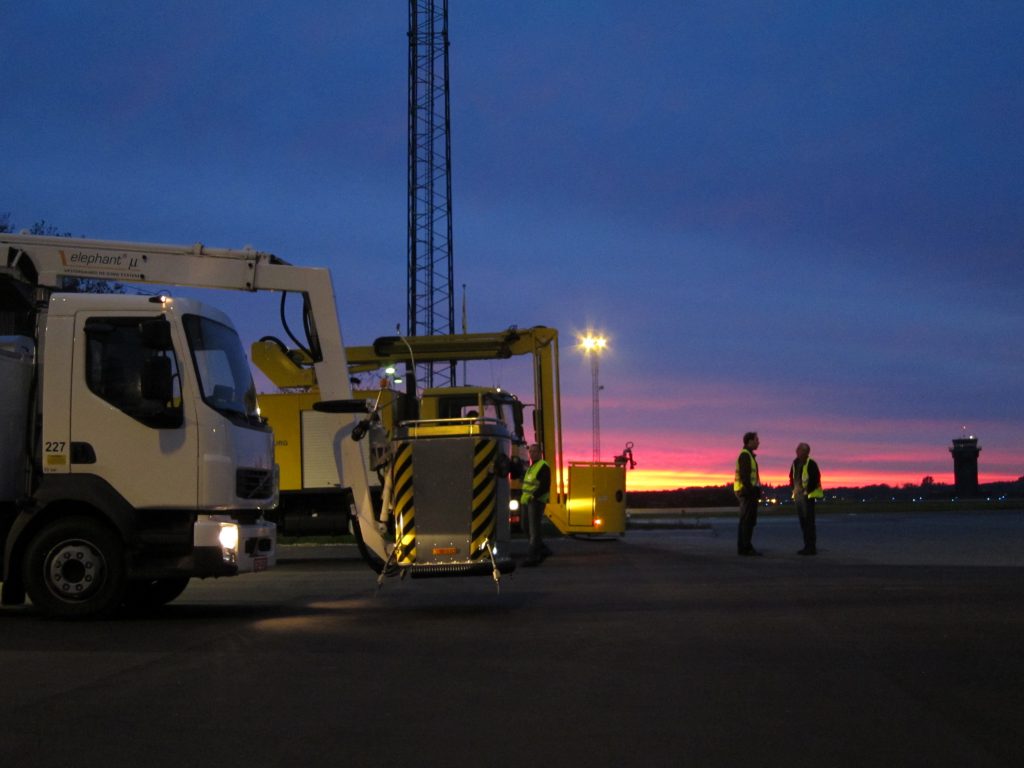 Trucks and equipment at dusk, with workers preparing for operations against a colorful sunset backdrop.