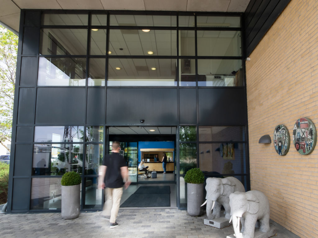 Entrance of a modern building with large glass doors, a person walking in, and decorative elephant sculptures outside.