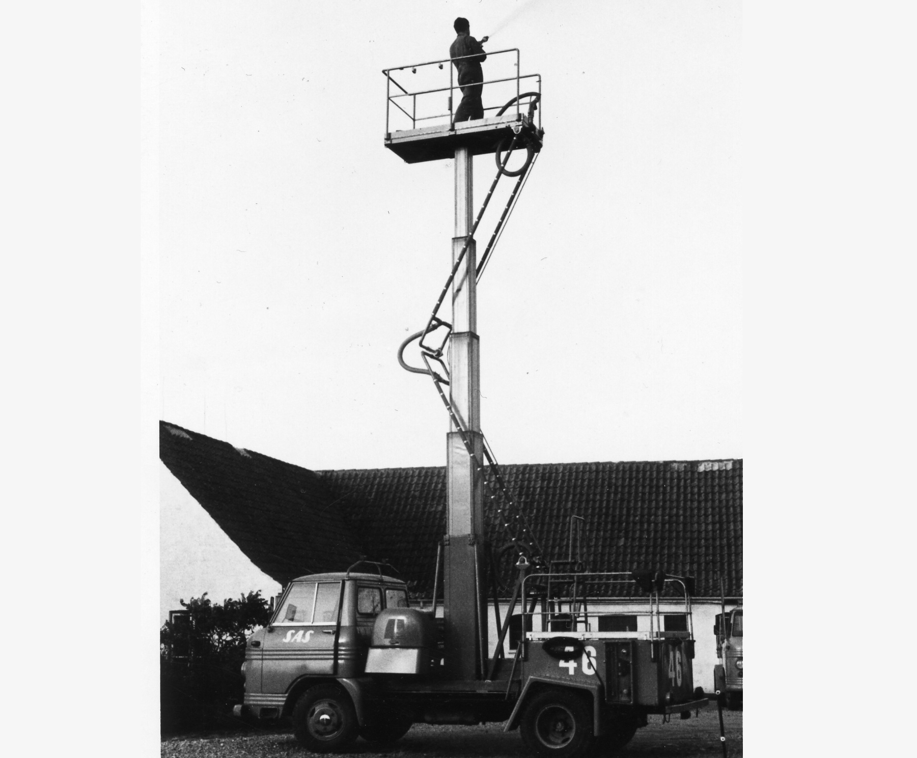 A worker stands on a raised platform of a lift, positioned next to a building, with equipment visible below.