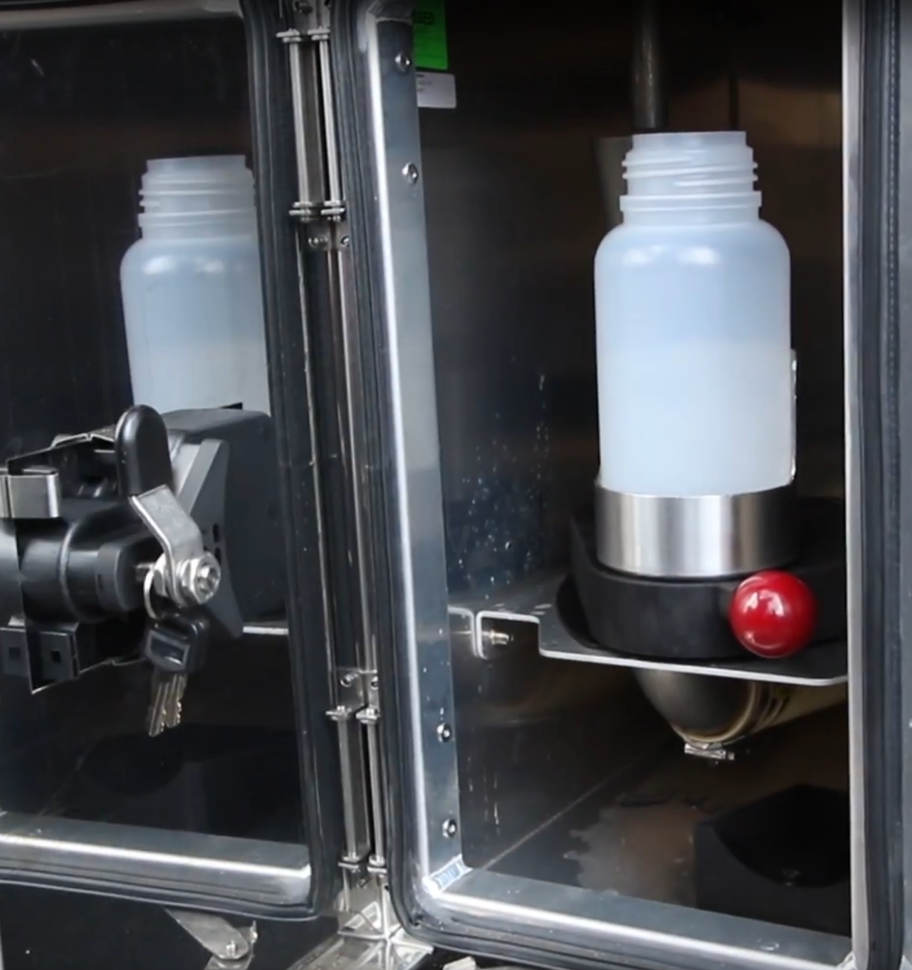 Transparent bottles inside a metal dispenser, with a red button and a key lock mechanism visible.