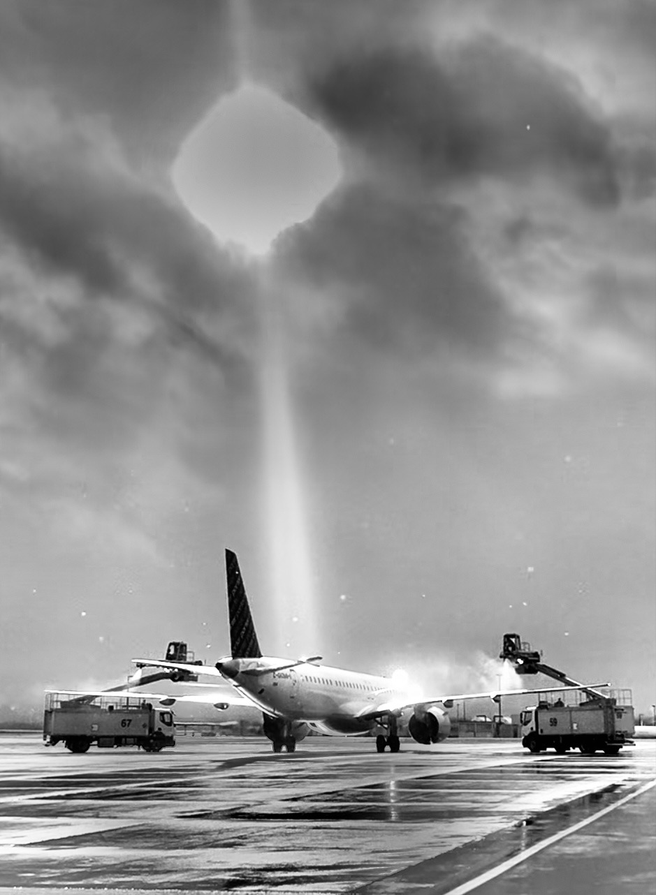 Airplane on a wet runway with two service vehicles, one labeled "67" and the other "59," under cloudy skies.