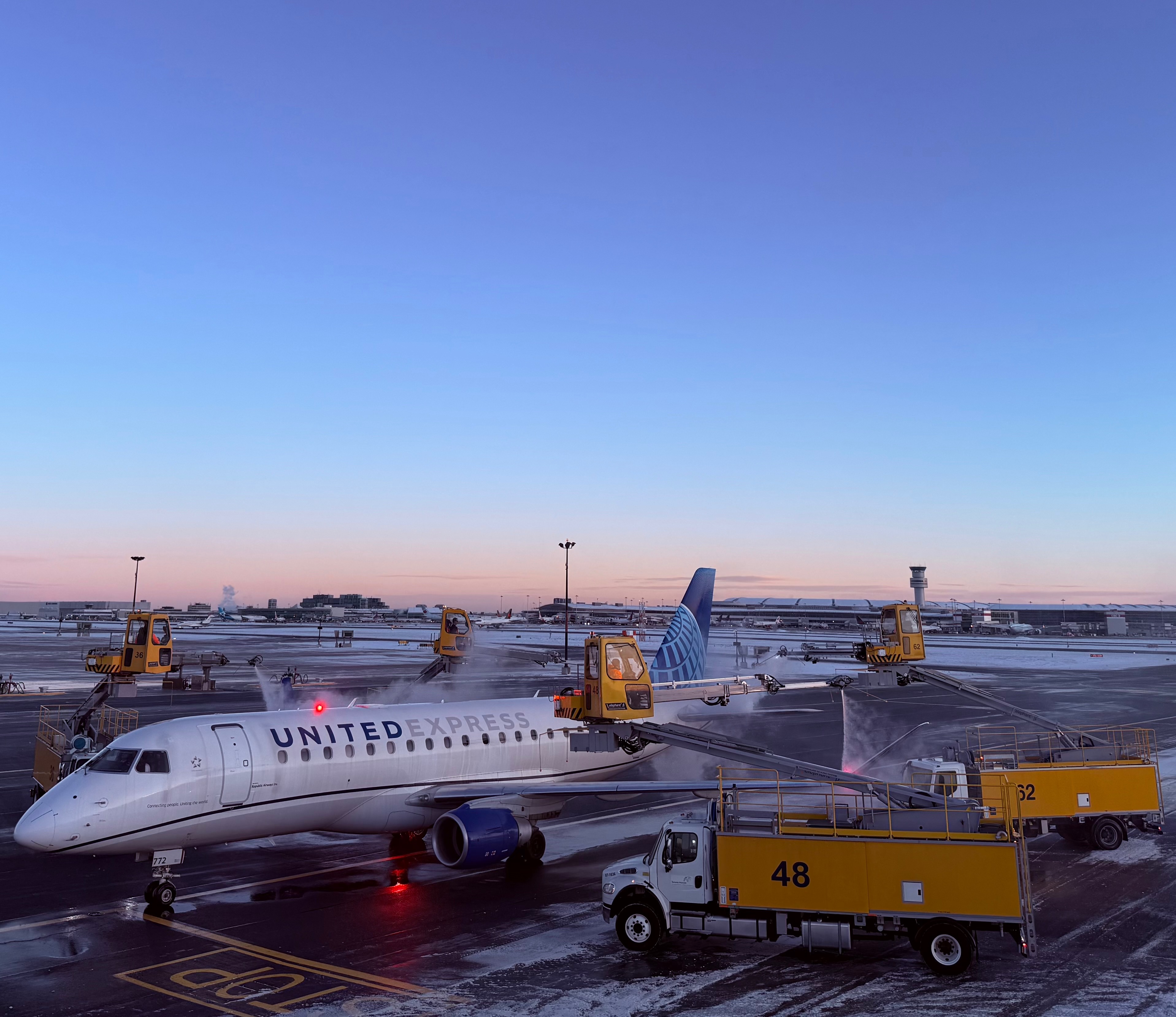 United Express aircraft being serviced at the airport with de-icing trucks labeled 48 and 52 in the foreground.