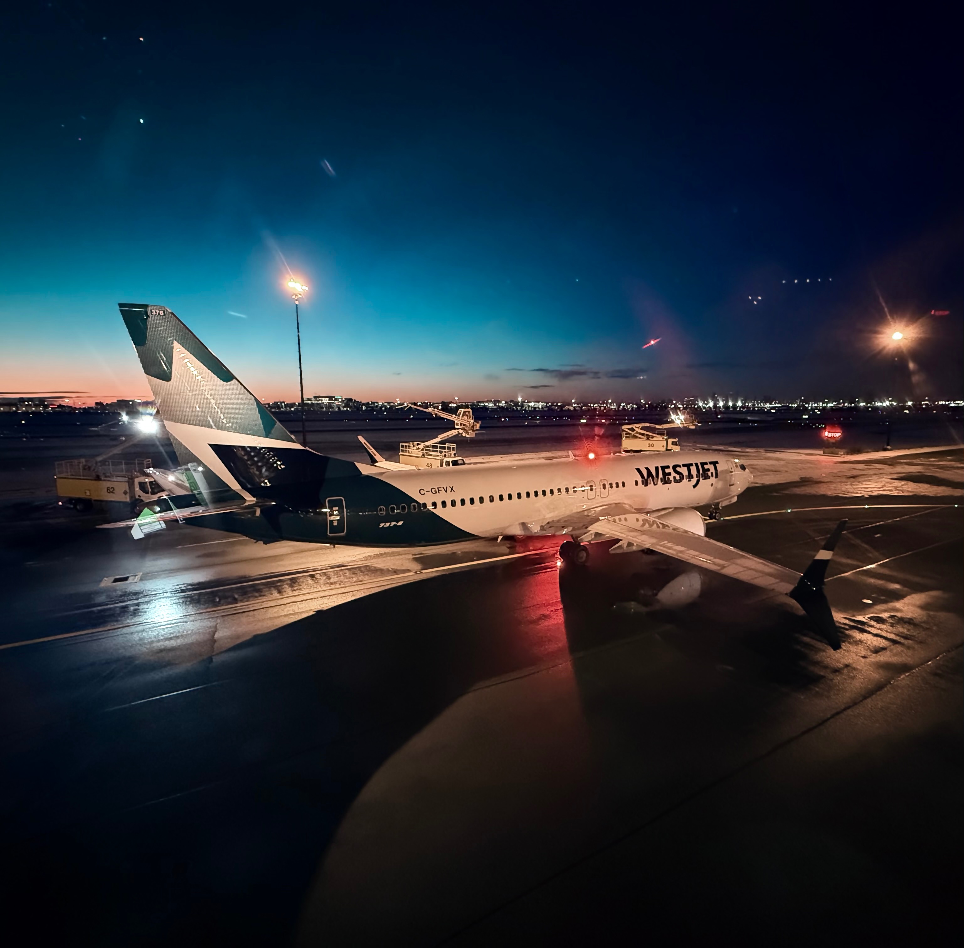 WestJet airplane with registration C-GFVX on a runway at dusk, illuminated by airport lights.