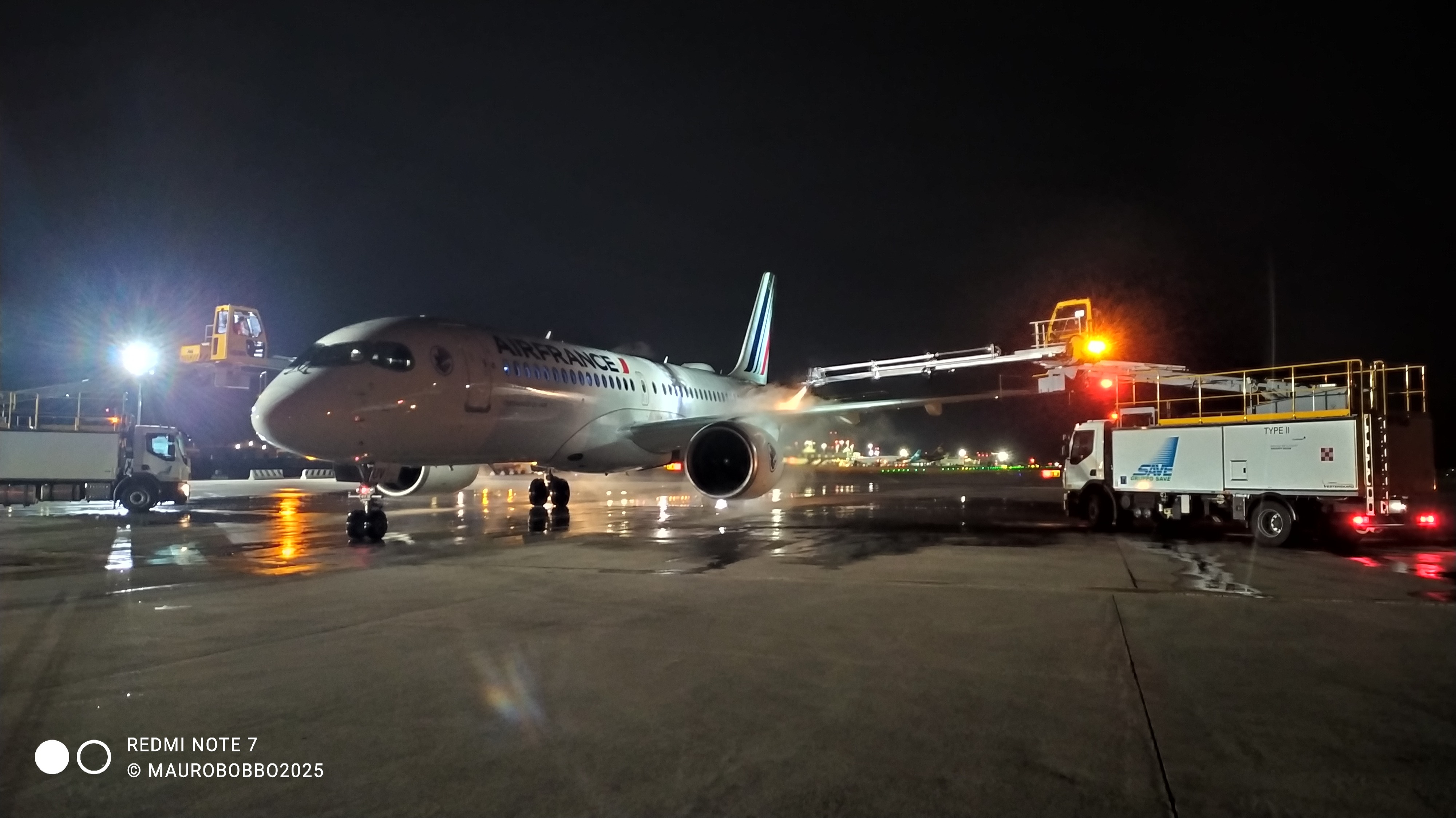 Air France aircraft on the tarmac at night, with a service truck and maintenance lift in operation.