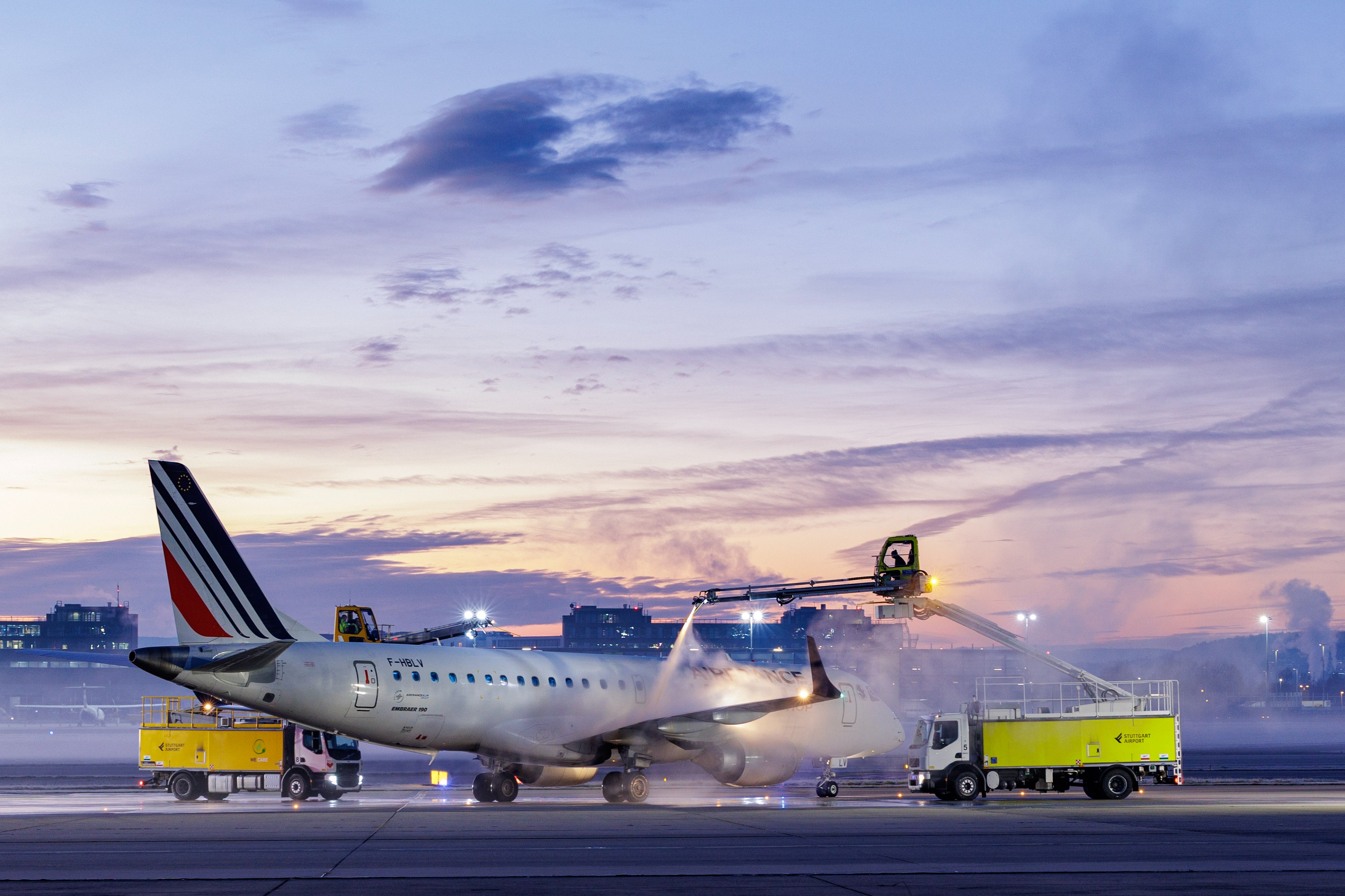 Airplane being serviced on the runway at sunset, with a truck and lift spraying the aircraft.